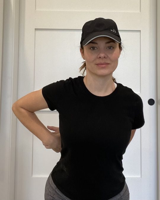 Elizabeth Chappell in a black hat and black shirt stretching her arms