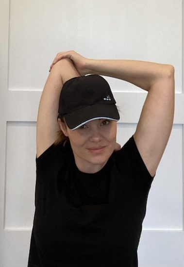 Elizabeth Chappell in a black hat and black shirt stretching her arms