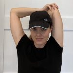 Elizabeth Chappell in a black hat and black shirt stretching her arms