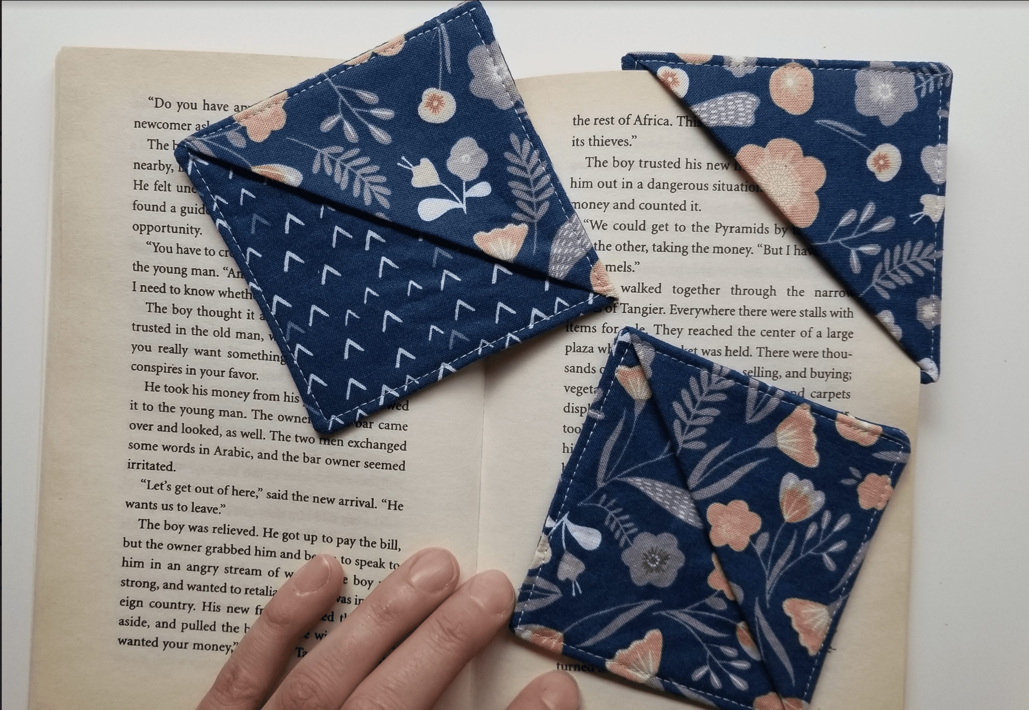 3 fabric book marks made of blue fabric, one being used to hold a book's spot