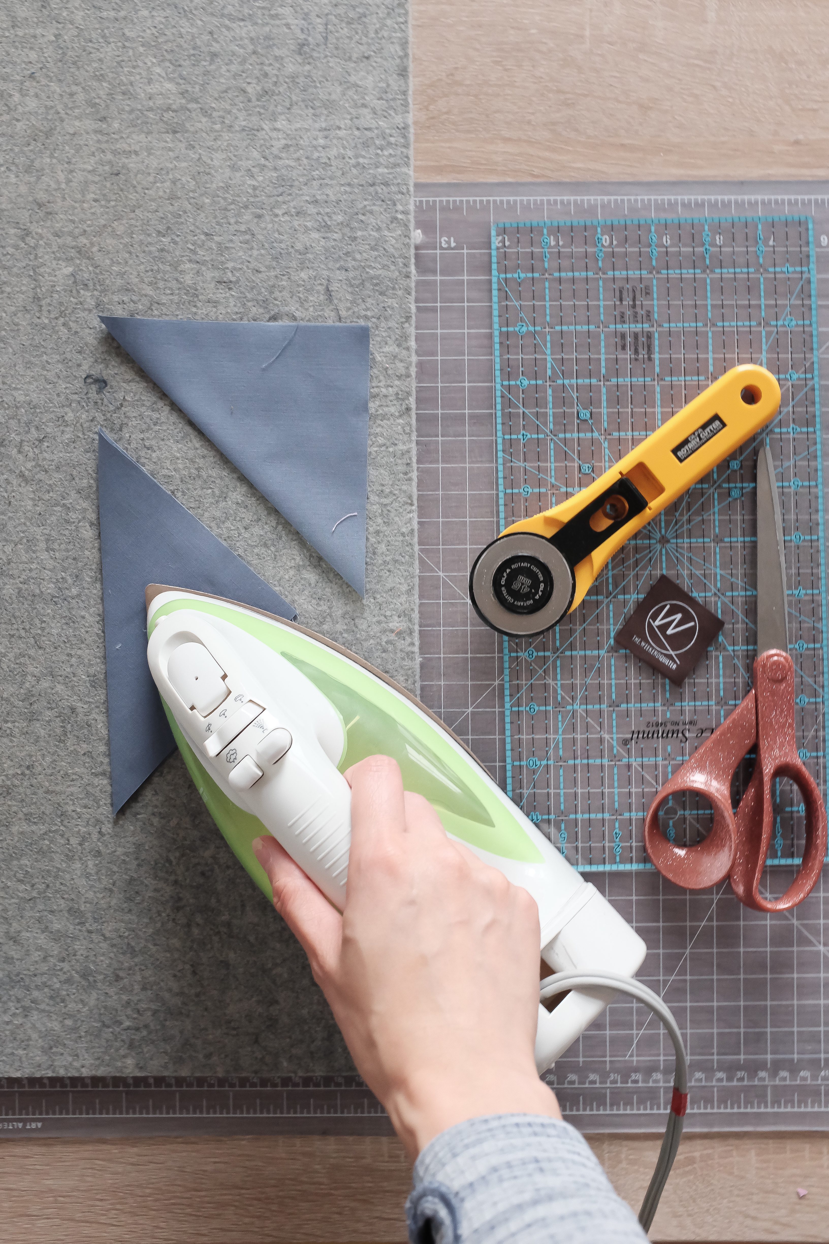 An iron pressing fabric in half, a rotary cutter, and scissors.