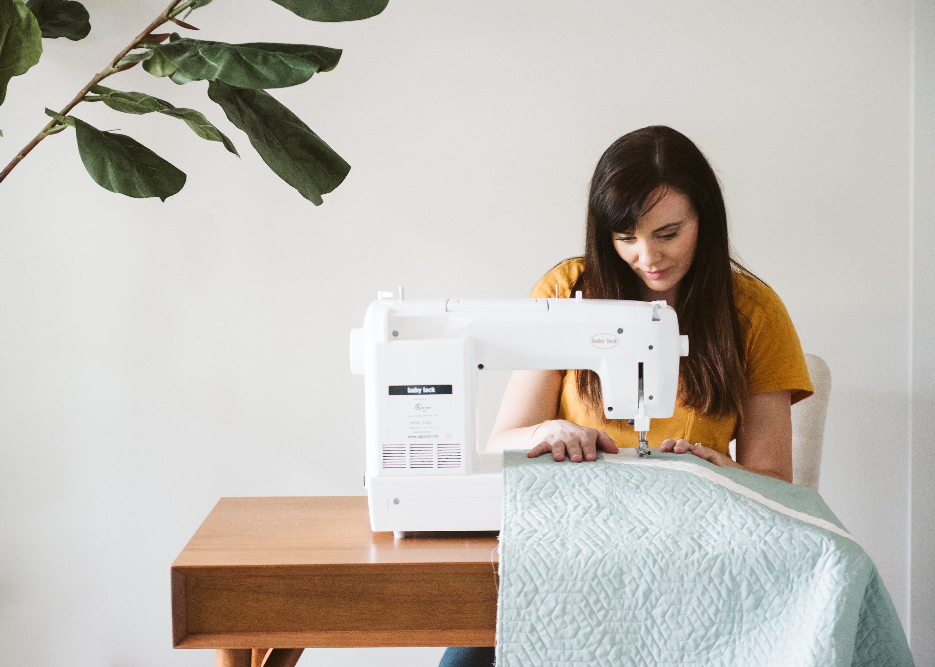 brown haired girl sewing a blue quilt on a sewing machine