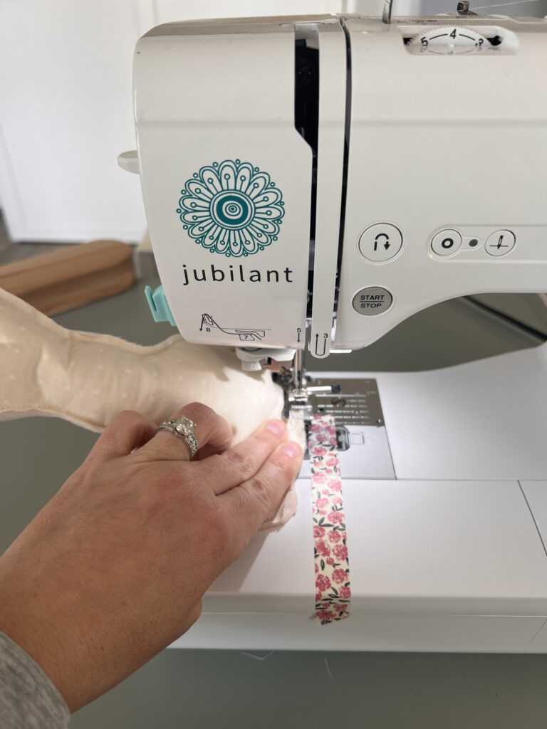 A fabric bunny is being sewn by a sewing machine branded Baby Lock Jubilant.