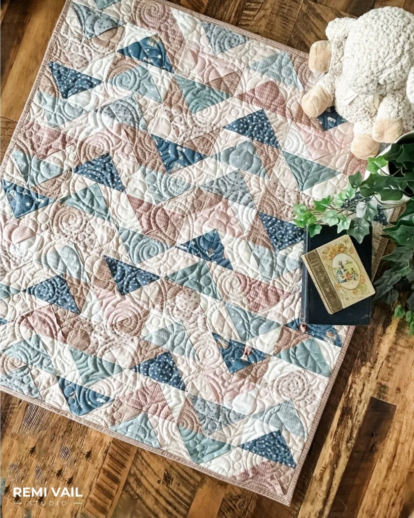 a quilt top with blues, pinks, and browns, on a wooden table top.