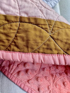 Close-up of quilted fabric showing white quilting stitches on mustard and pink fabric, highlighting how thread weight and color affect the look of quilting.