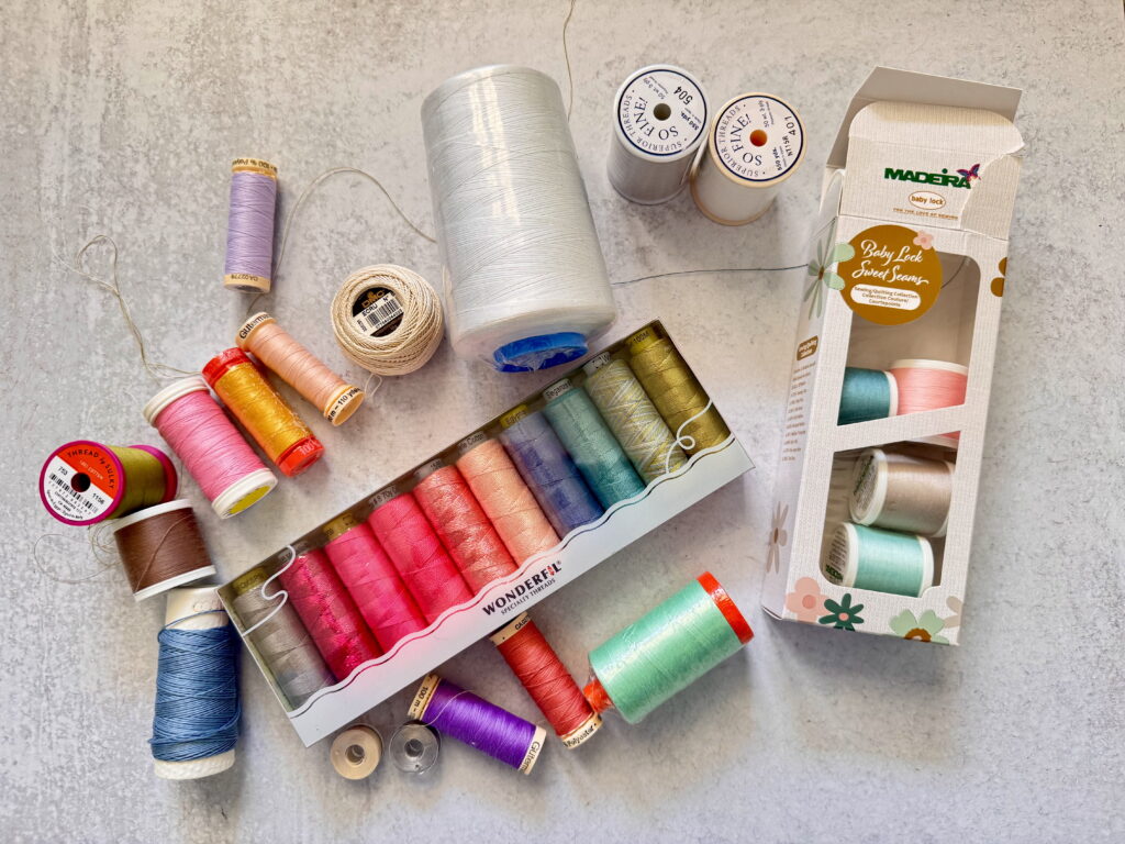 Assortment of quilting threads in multiple colors and brands, showing the range of thread weights used for quilting projects.