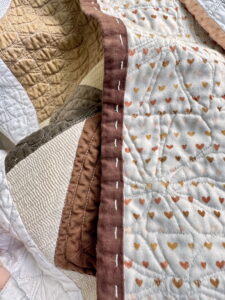 Quilt binding hand-stitched with brown thread, showing how heavier thread weight creates a visible, rustic quilting finish.