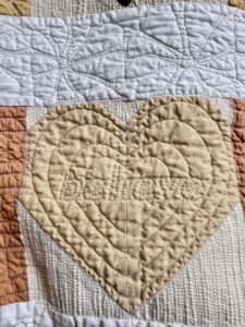 Close-up of quilt with stitched heart and the word “believe,” demonstrating how thread choice can highlight decorative quilting designs.