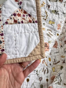 Close-up of quilted fabric showing white quilting stitches on mustard and pink fabric, highlighting how thread weight and color affect the look of quilting.