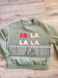 Green FA LA LA appliqué sweatshirt with a quilting ruler used to align the letters before sewing.