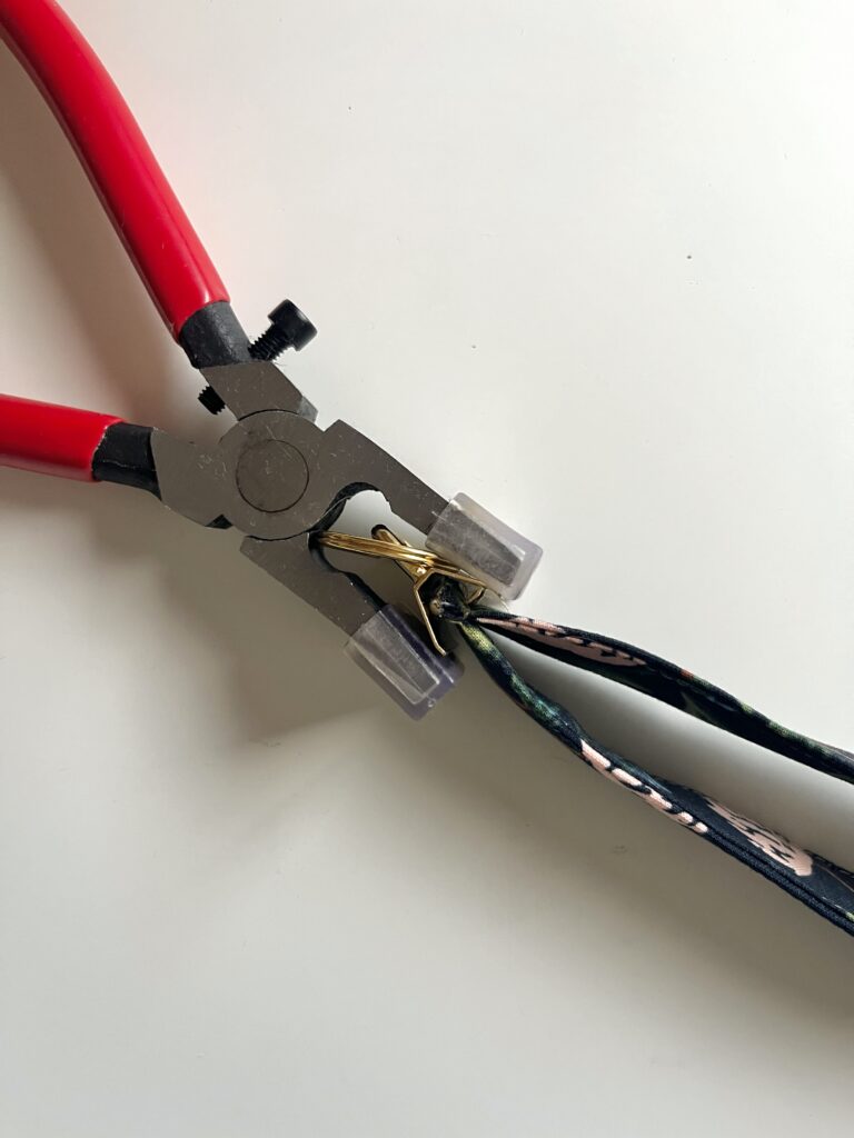 Key fob pliers squeezing gold hardware closed over the end of a fabric wristlet