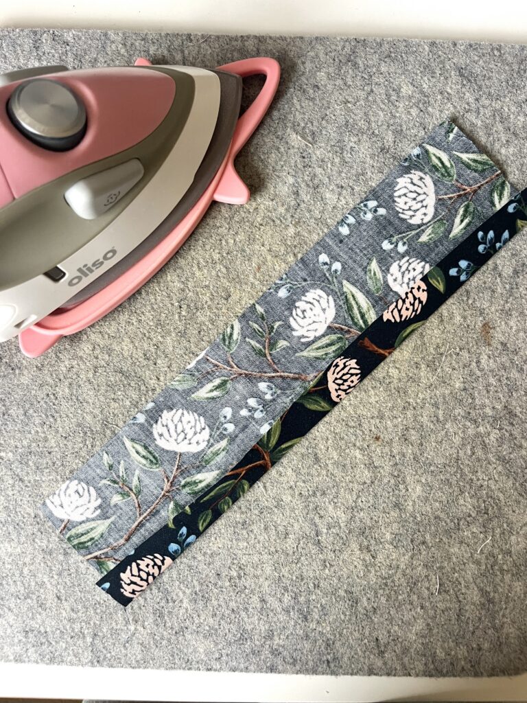 Long raw edges of a fabric strip folded in to meet the center crease and pressed