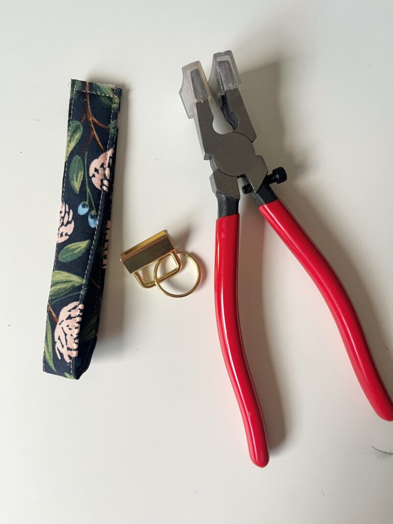 Sewn fabric wristlet loop next to gold key fob hardware and red-handled key fob pliers