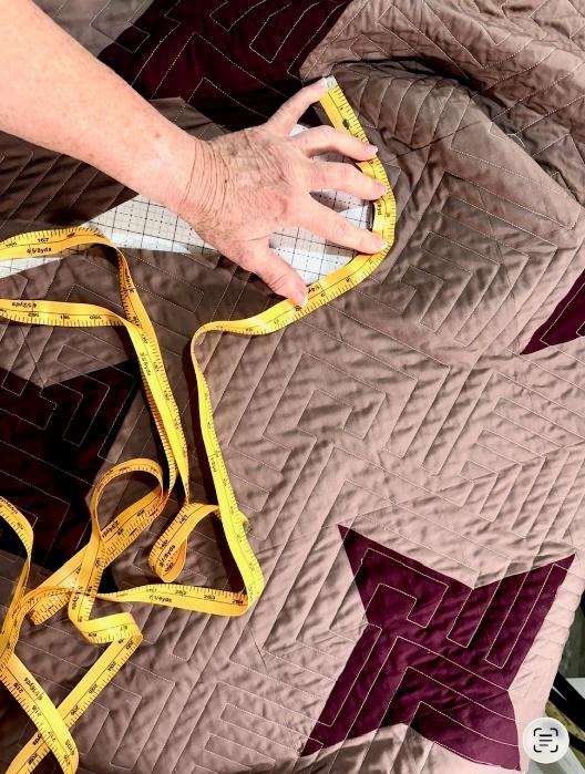 Measuring the curved neckline of a quilted ruana with yellow measuring tape